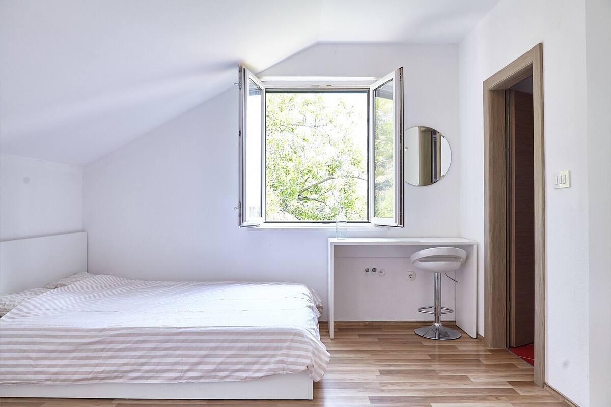 Una camera da letto con un letto, una scrivania con una sedia, uno specchio e una finestra vista alberi.