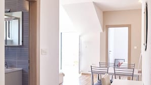 A modern kitchen with a built-in oven, a dining area with a table and chairs, and a hallway leading to a bedroom.