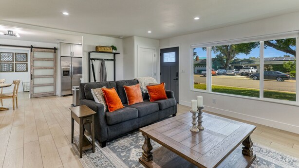 A modern living room with a dark grey sofa, wooden coffee table, and a view of a parking lot through large windows. - ***Carpenter Lane*** (Redding)