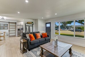 A modern living room with a dark grey sofa, wooden coffee table, and a view of a parking lot through large windows. - ***Carpenter Lane*** (Redding)