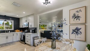 A modern kitchen with white cabinets, a microwave, and a stove. There is a dining table with chairs and a vase with flowers. - ***Carpenter Lane*** (Redding)