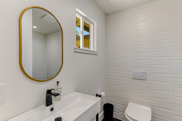 A bathroom with a white sink, a gold-framed mirror, a window, and a textured wall. - ***Carpenter Lane*** (Redding)
