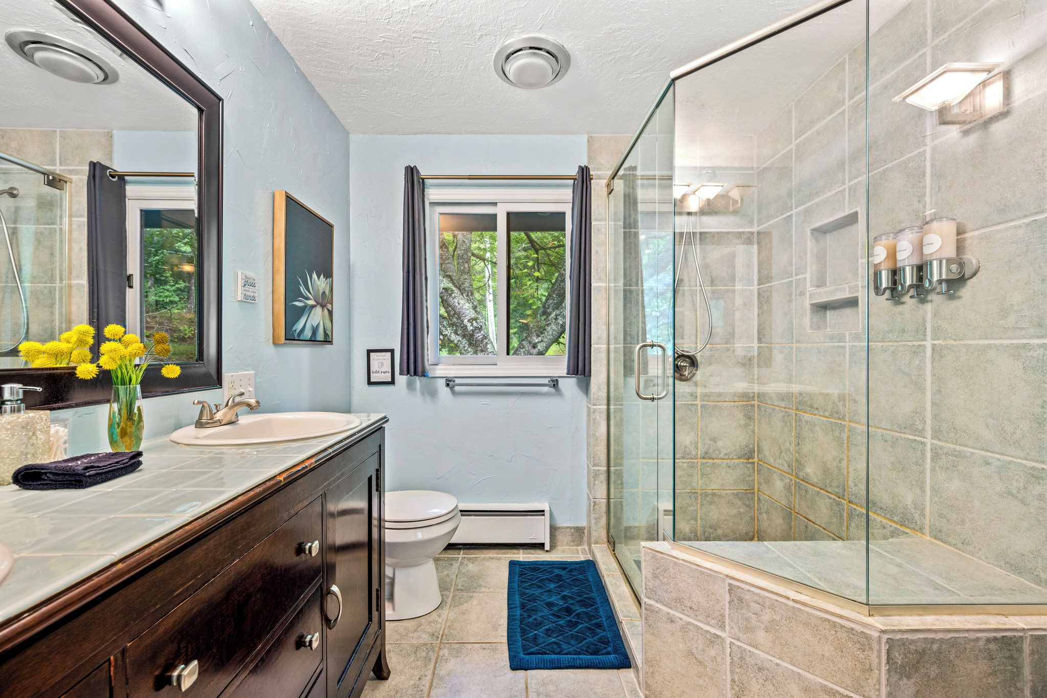 A bathroom with a glass shower enclosure, a sink, a toilet, and a window with curtains.