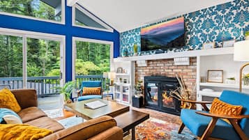 A modern living room with a fireplace, blue walls, and a large window overlooking a deck.