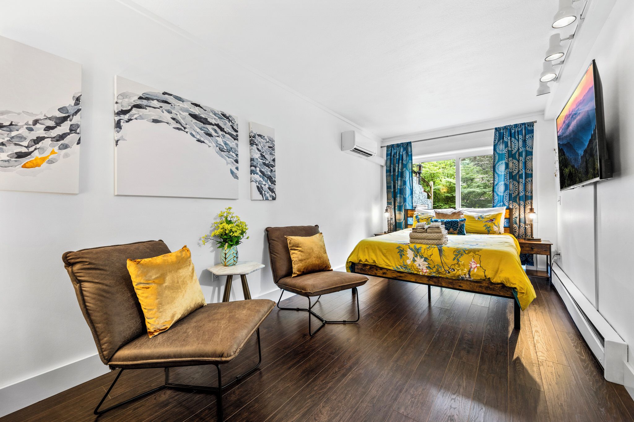 A modern hotel room with a bed, two armchairs, a small table, and artwork on the walls.