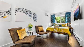 A modern hotel room with a bed, two armchairs, a small table, and artwork on the walls.