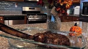 Una cocina con armarios de madera, un microondas, un horno y un recipiente de vidrio con carne asada como plato principal.