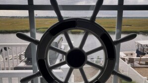 Una rueda de barco fijada en una pared, con vista a un aeropuerto al fondo.