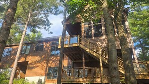 A multi-story wooden cabin with a balcony and large windows, surrounded by tall trees. - Muskoka Waterfront Cottage on 54 acres, 10 minutes from Gravenhurst (Gravenhurst)