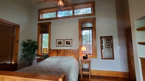 A bedroom with a large bed, wooden headboard, two windows with blinds, a bedside table with a lamp, and a potted plant. - Muskoka Waterfront Cottage on 54 acres, 10 minutes from Gravenhurst (Gravenhurst)
