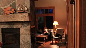 A cozy living room with a stone fireplace, wooden furniture, and a window with a view of the outside. - Muskoka Waterfront Cottage on 54 acres, 10 minutes from Gravenhurst (Gravenhurst)