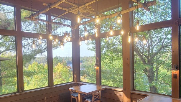 A wooden dining area with large windows, a ceiling fan, and hanging light bulbs. - Muskoka Waterfront Cottage on 54 acres, 10 minutes from Gravenhurst (Gravenhurst)