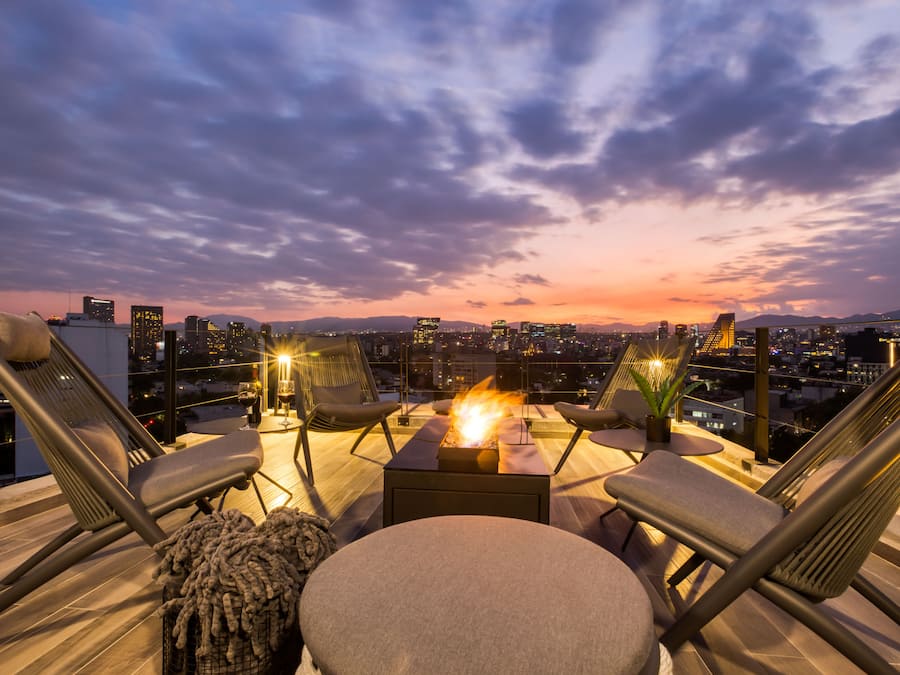 Terraza en la azotea con chimenea, asientos y vistas a la ciudad al atardecer.