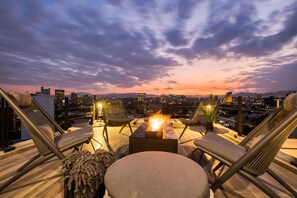 Terraza en la azotea con chimenea, asientos y vistas a la ciudad al atardecer.