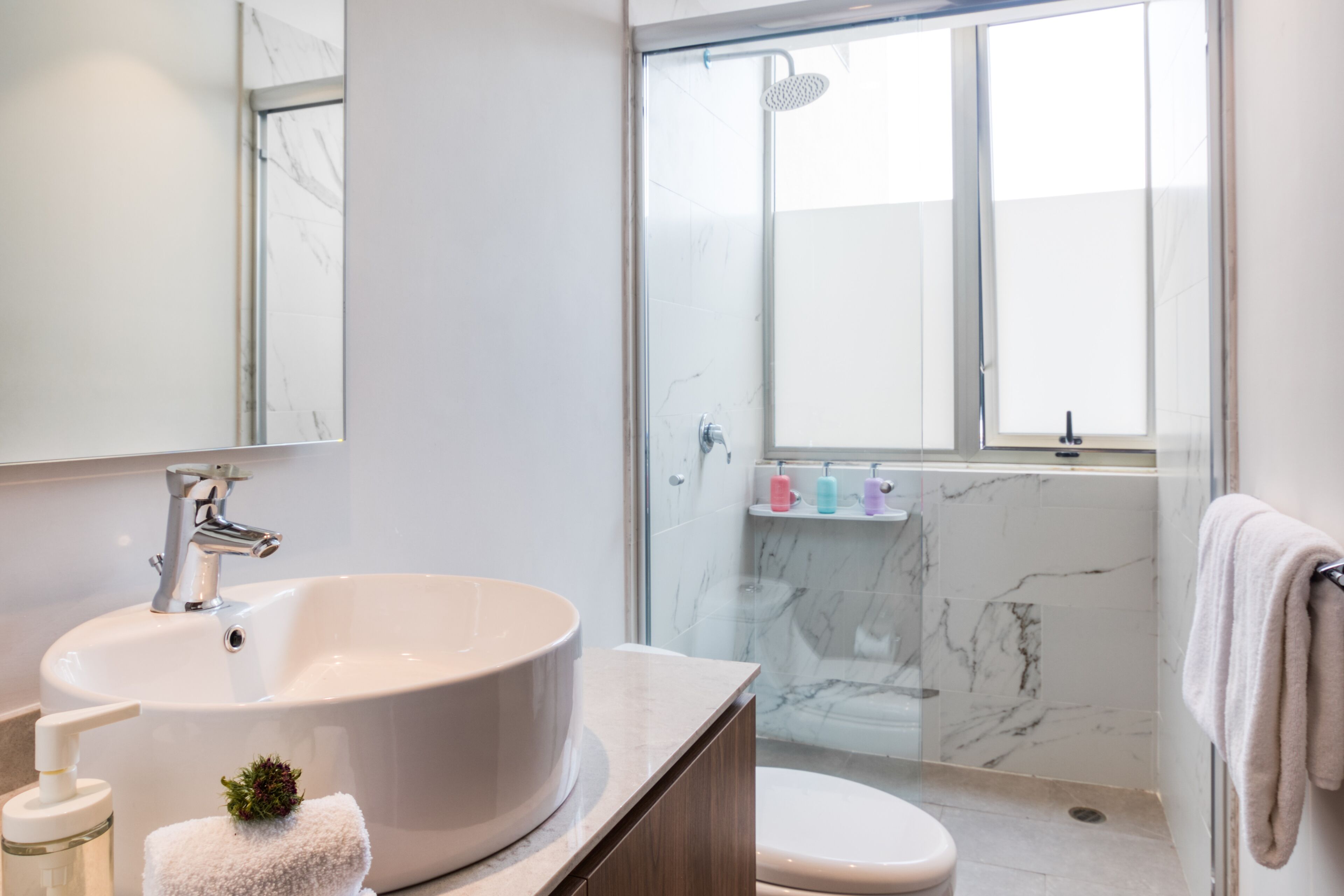 A modern bathroom with a large white sink, a glass shower enclosure, and a toilet.