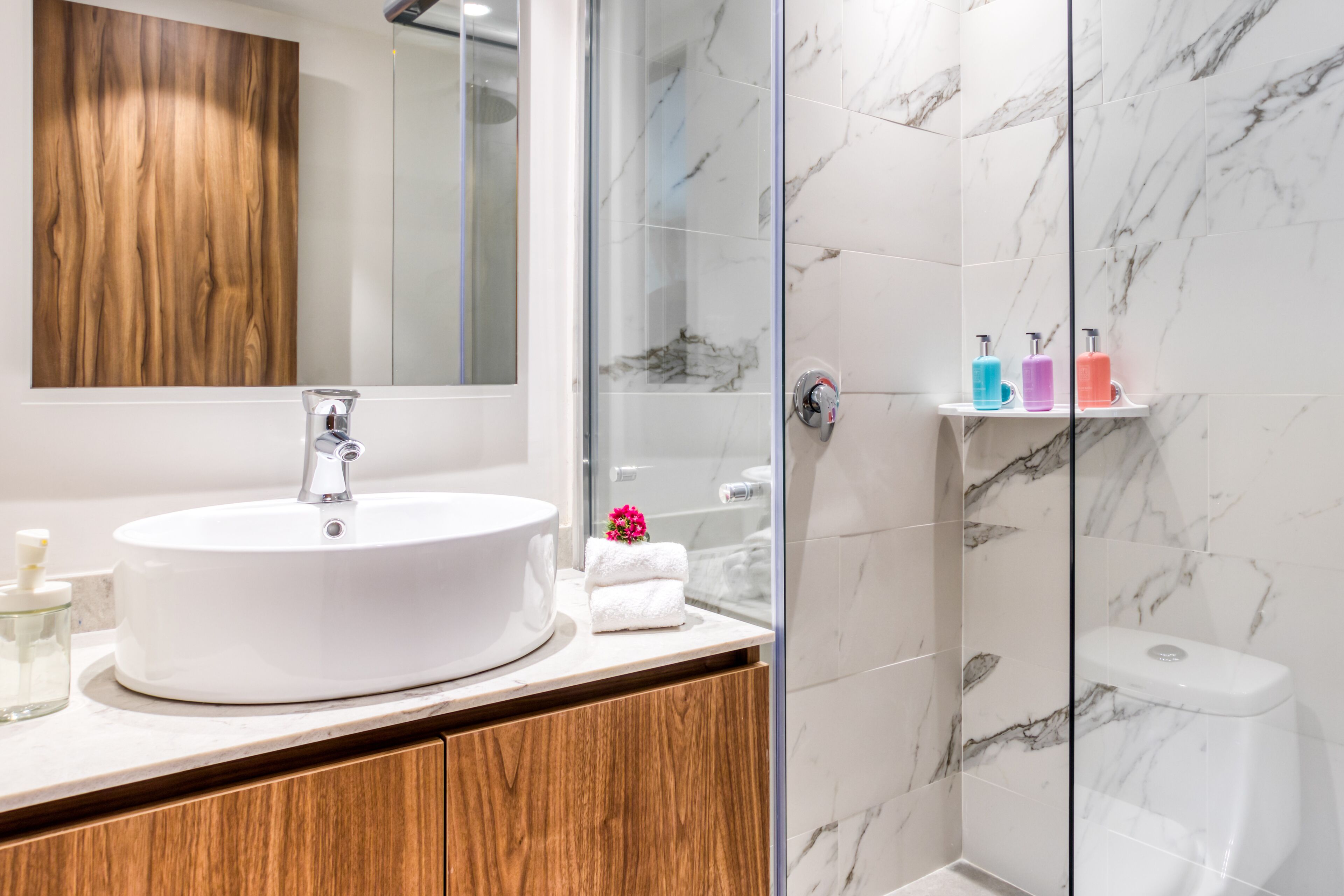 A bathroom with a white sink, wooden cabinet, marble shower walls, and a glass-enclosed shower.