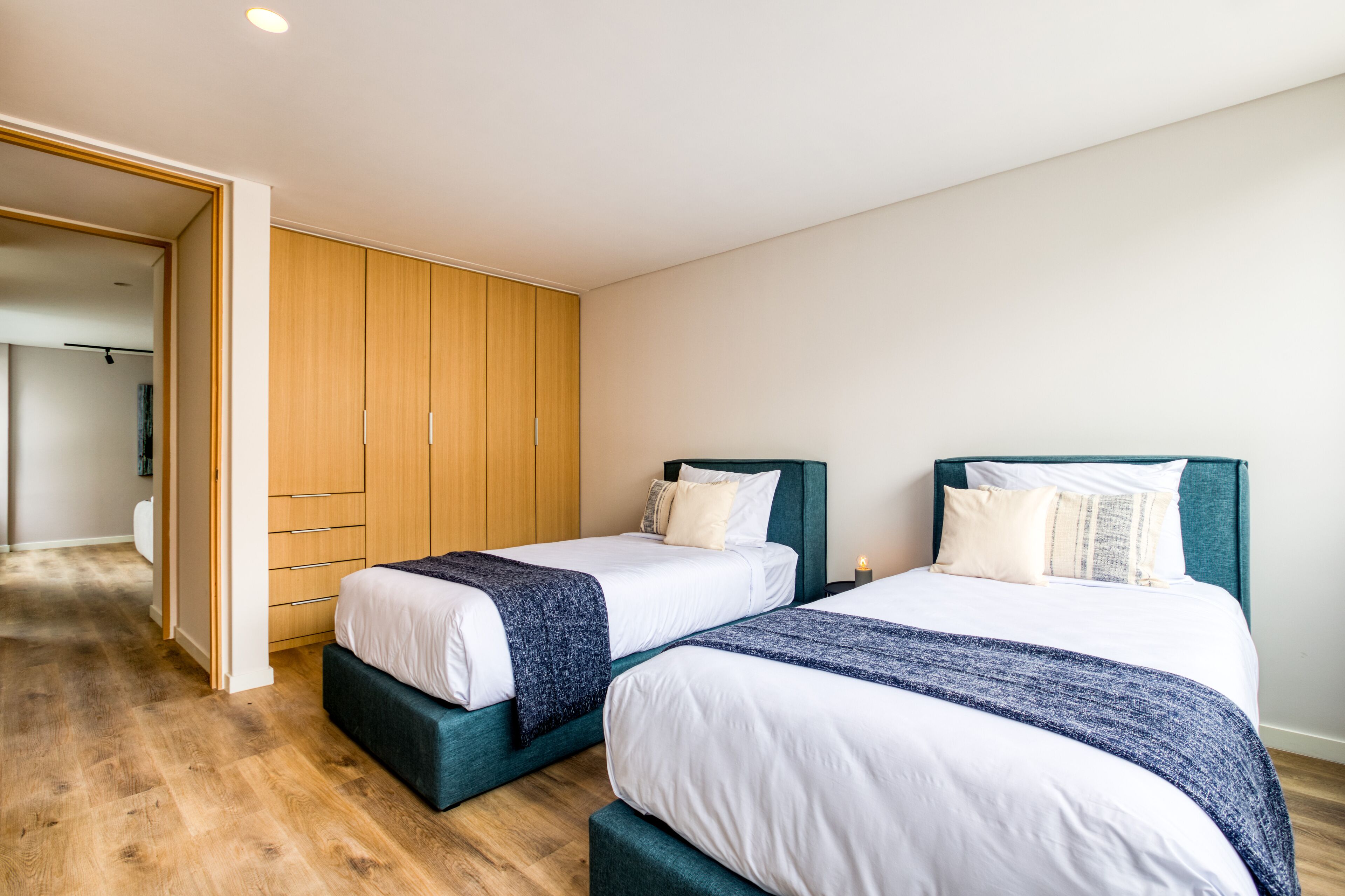 Une chambre avec deux lits, une armoire en bois et un couloir menant à une autre pièce.
