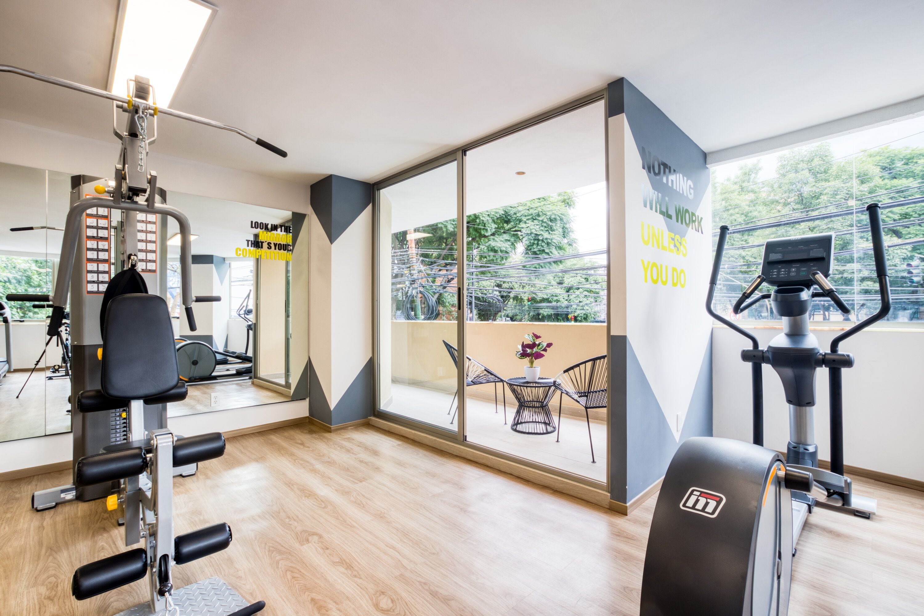 A modern gym with exercise equipment, large windows, and motivational wall art.