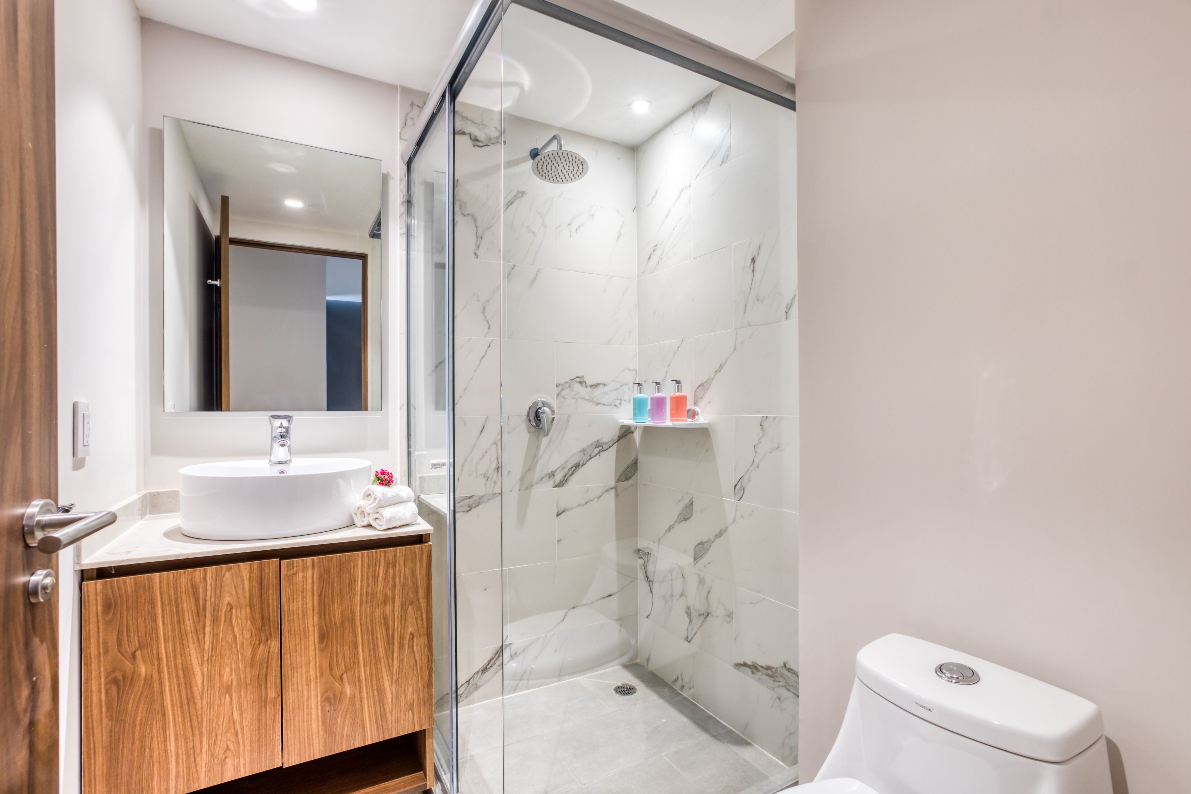 A modern bathroom with a glass-enclosed shower, a white sink, and a toilet.