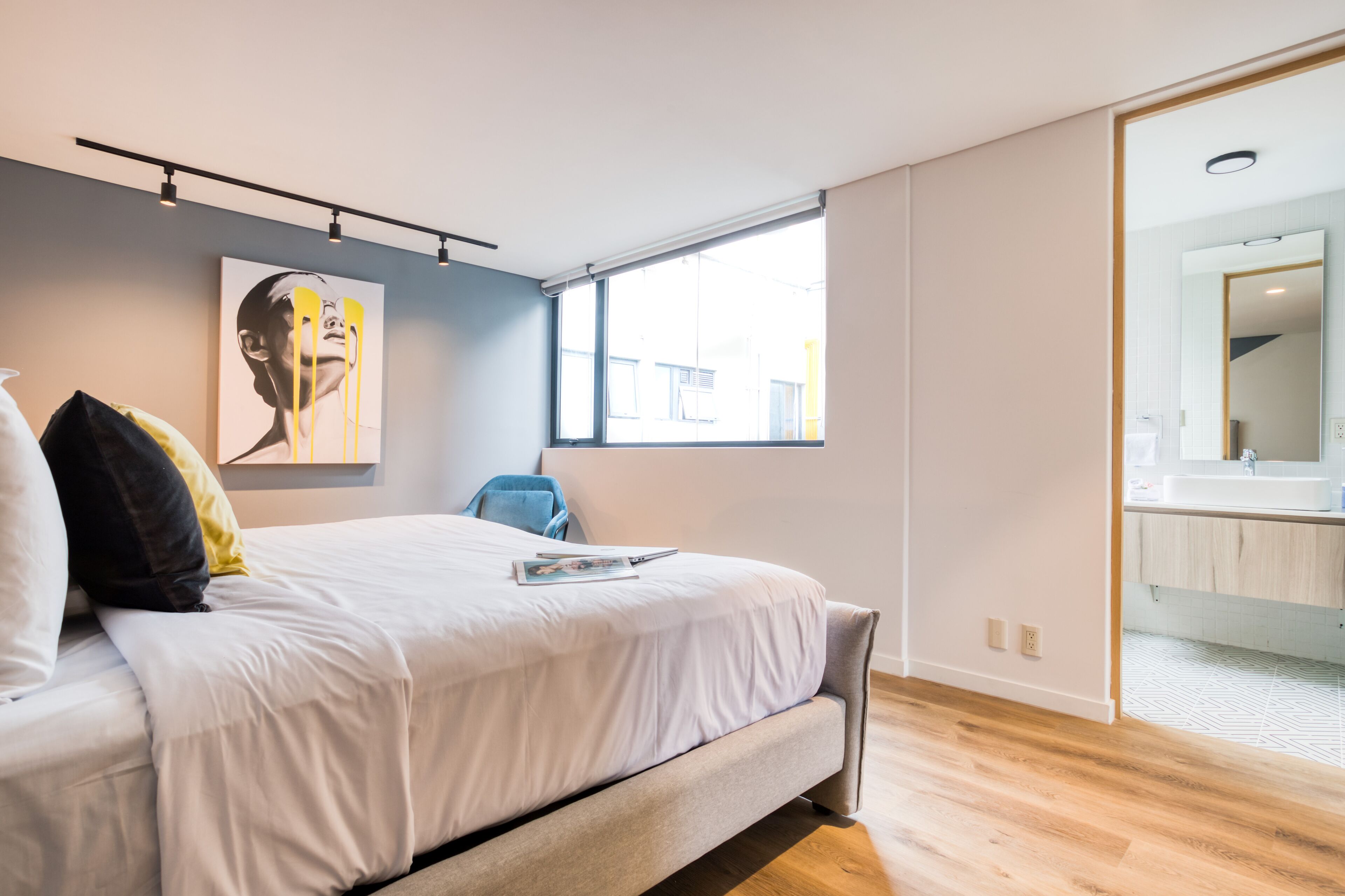 A modern bedroom with a large bed, a window, and a bathroom visible through an open door.