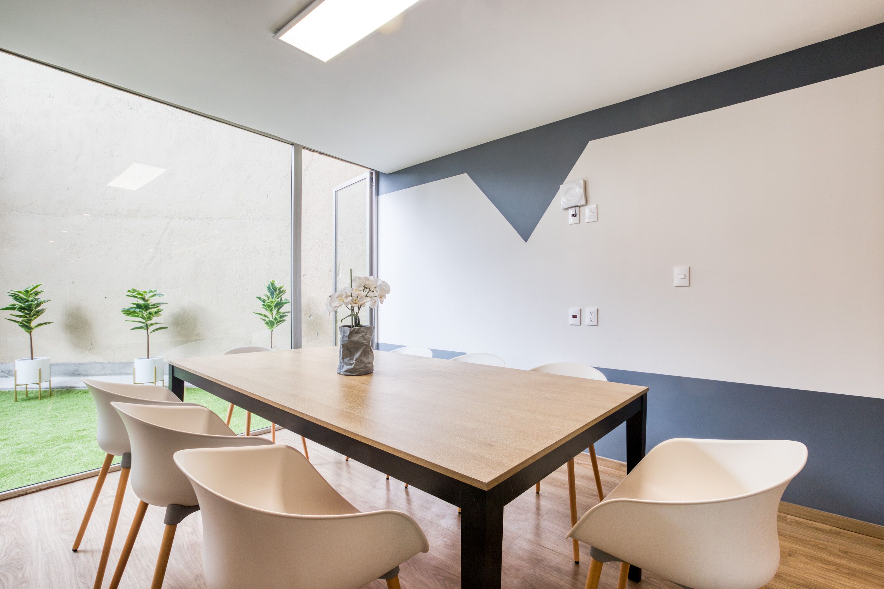 A conference room with a long table, six chairs, and a vase with flowers.