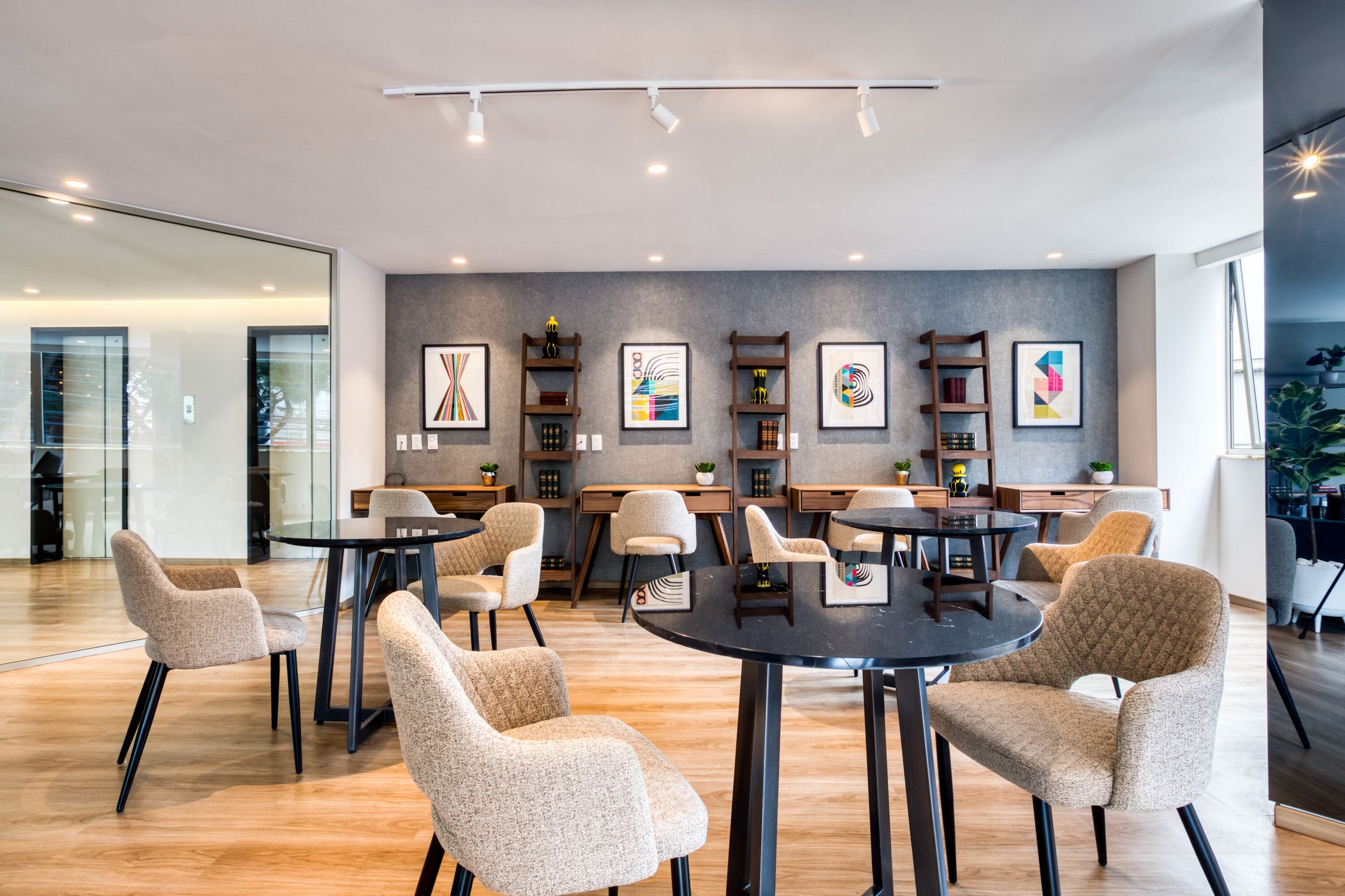 A modern interior with round tables and chairs, wooden shelves with artwork, and a glass wall.