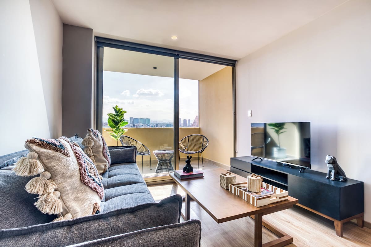 A modern living room with a sofa, a coffee table, a TV, and a balcony with a city view.