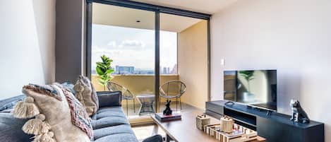 Uma sala de estar moderna com sofá, mesa de centro, TV e varanda com vista para a cidade.