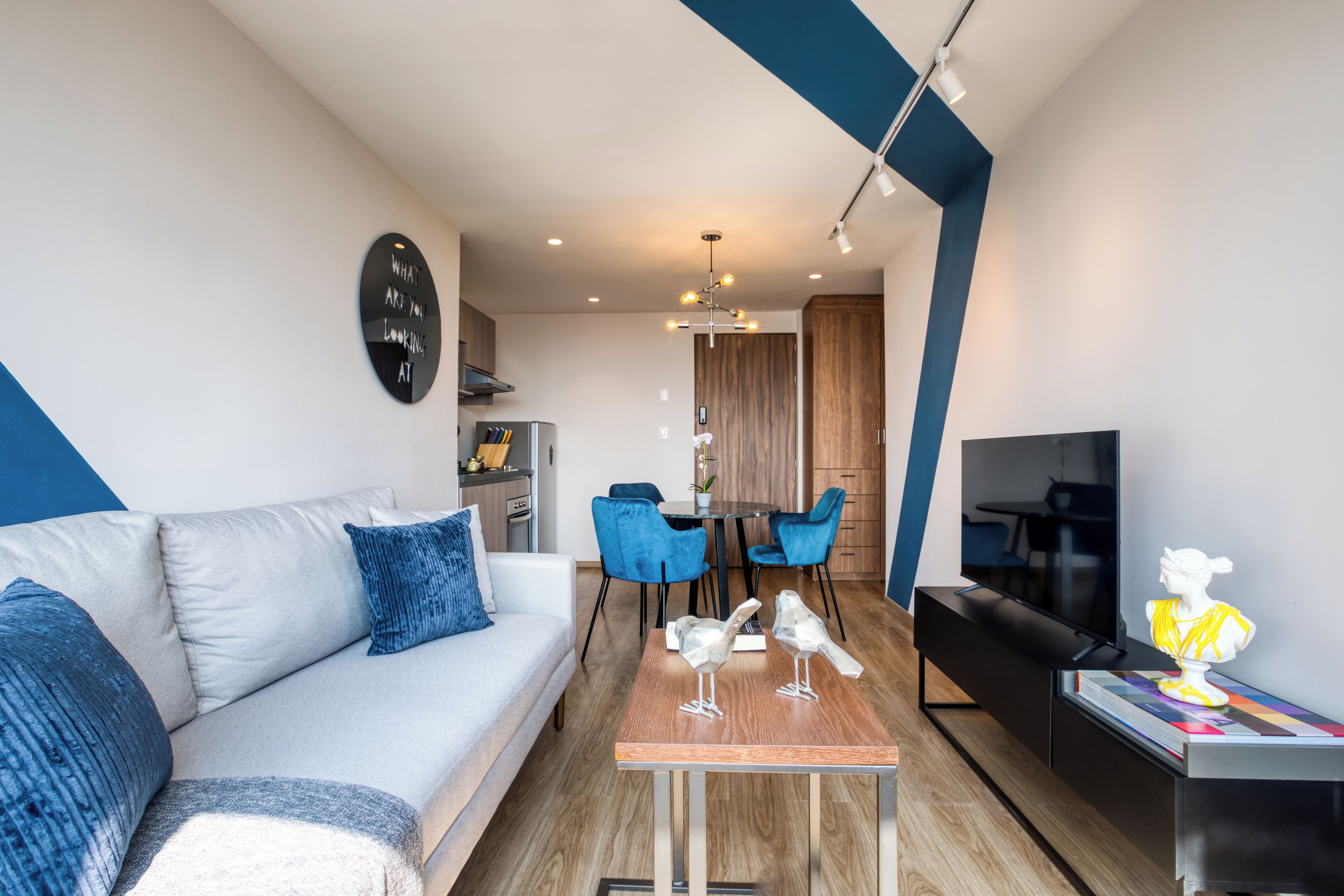 Una sala de estar moderna con un sofá, una mesa de centro y un televisor. Hay una zona de comedor con sillas y una mesa.