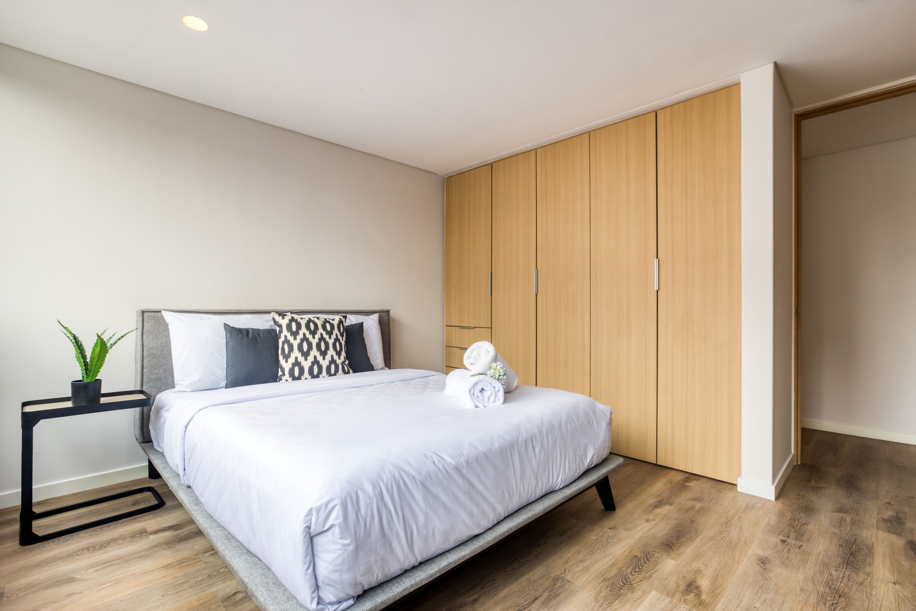 Un dormitorio moderno con cama, mesita de noche, planta en maceta y armario.