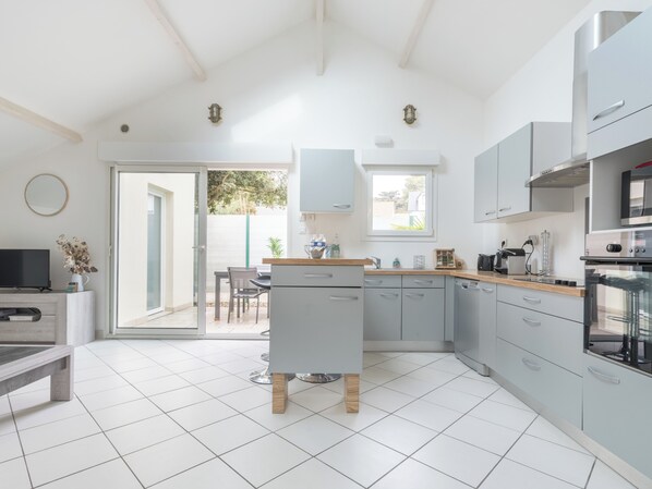 A modern kitchen with a central island, built-in appliances, and a dining area with a view. - MARGUERITE - Wifi - Parking (Pornichet)