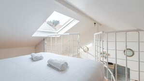 Een slaapkamer met dakraam, een bed met opgerolde handdoeken, een witte metalen leuning en uitzicht op het buiten.