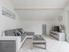 A modern living room with a grey sectional sofa, a coffee table, a TV on a wooden stand, and a painting on the wall. - MARGUERITE - Wifi - Parking (Pornichet)