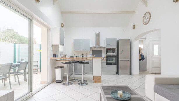 Een moderne keuken met een centraal eiland, barkrukken, een koelkast en een zithoek met een bank en tafel.