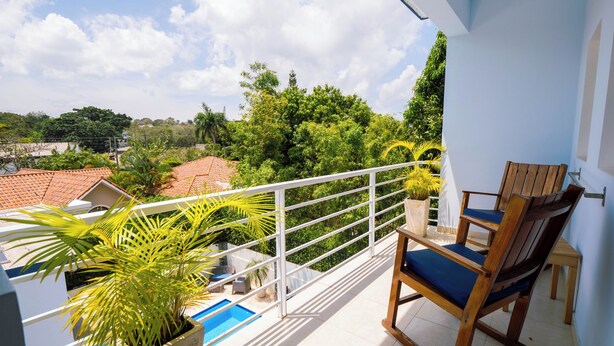 A balcony with a view of a swimming pool, a wooden chair, and potted plants.