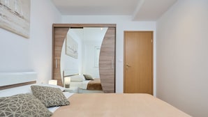 A bedroom with a bed, two patterned pillows, a wooden door, and a mirror reflecting a bathroom with a bathtub and a sofa. - Hedera Estate, Hedera A38 (Dubrovnik)