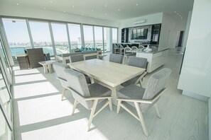 A spacious dining area with a large table and chairs, a kitchen with modern appliances, and large windows offering a view of the city and beach. - Torre eMe Penthouse Oceanview Condo #1507 with Pool (Mazatlán)