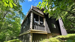 A rustic wooden cabin with a balcony, surrounded by lush greenery and trees. - North House - over 100 acres of Adirondack privacy! (Jay)