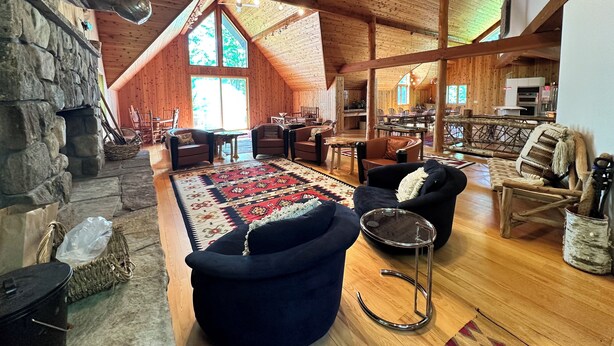 A spacious loft-style room with a stone fireplace, wooden ceiling beams, and a large window. - North House - over 100 acres of Adirondack privacy! (Jay)