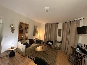 A cozy living room with a sofa, a coffee table, a bookshelf, and a dining area.