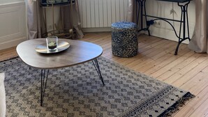 A room with a round table, a leopard print ottoman, a radiator, a TV on the wall, and a window with curtains.