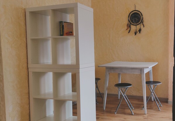 Ein Zimmer mit einem weißen Bücherregal, einem Tisch und zwei Hocker.