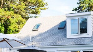 A residential swimming pool with a patio area, a covered seating arrangement, and a house with a gabled roof and large windows. - The Blue Crab Unit 7 (Harwich)