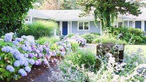 A house with a blue door, surrounded by a garden with hydrangeas and other plants. - The Blue Crab Unit 7 (Harwich)