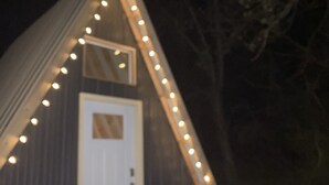 Un edificio triangular con una puerta blanca y luces colgantes a lo largo del borde del techo.