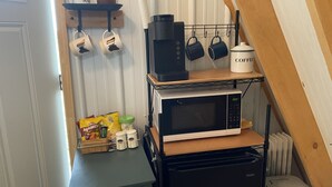 Una kitchenette compacta con microondas, cafetera y estantes para guardar objetos.