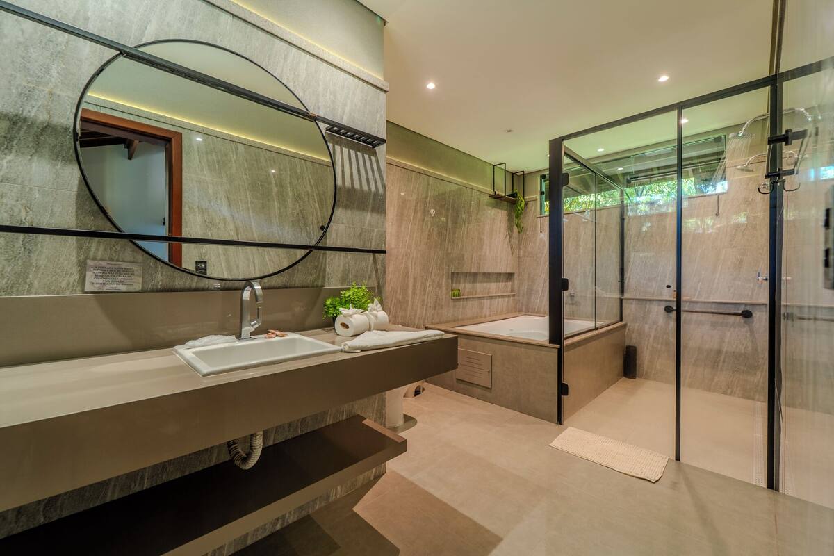 Un baño moderno con un espejo grande, dos lavamanos, una cabina de ducha y una planta pequeña en el mueble del lavabo.