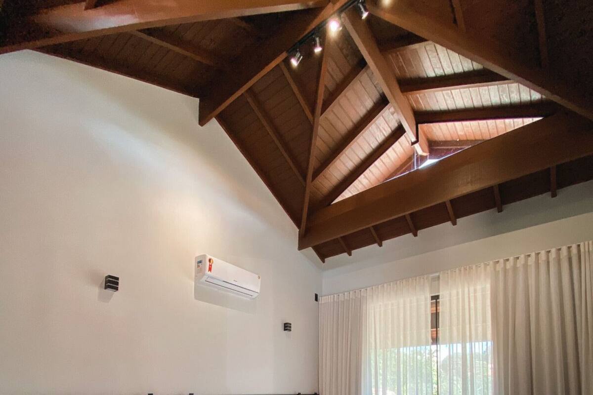 Habitación de hotel con dos camas, vigas de madera en el techo, un equipo de aire acondicionado y vistas a través de un ventanal con cortinas.
