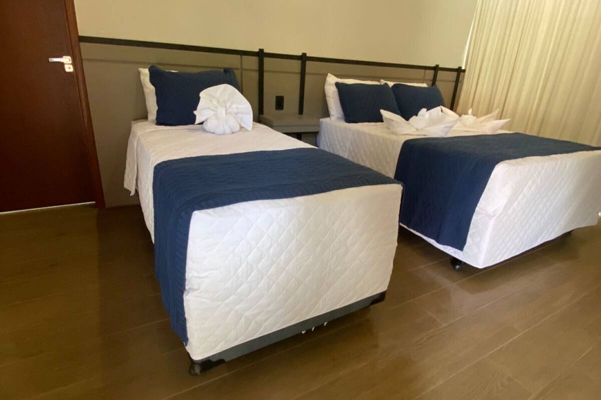 Habitación de hotel con dos camas, suelo de madera, aire acondicionado de pared y una puerta.