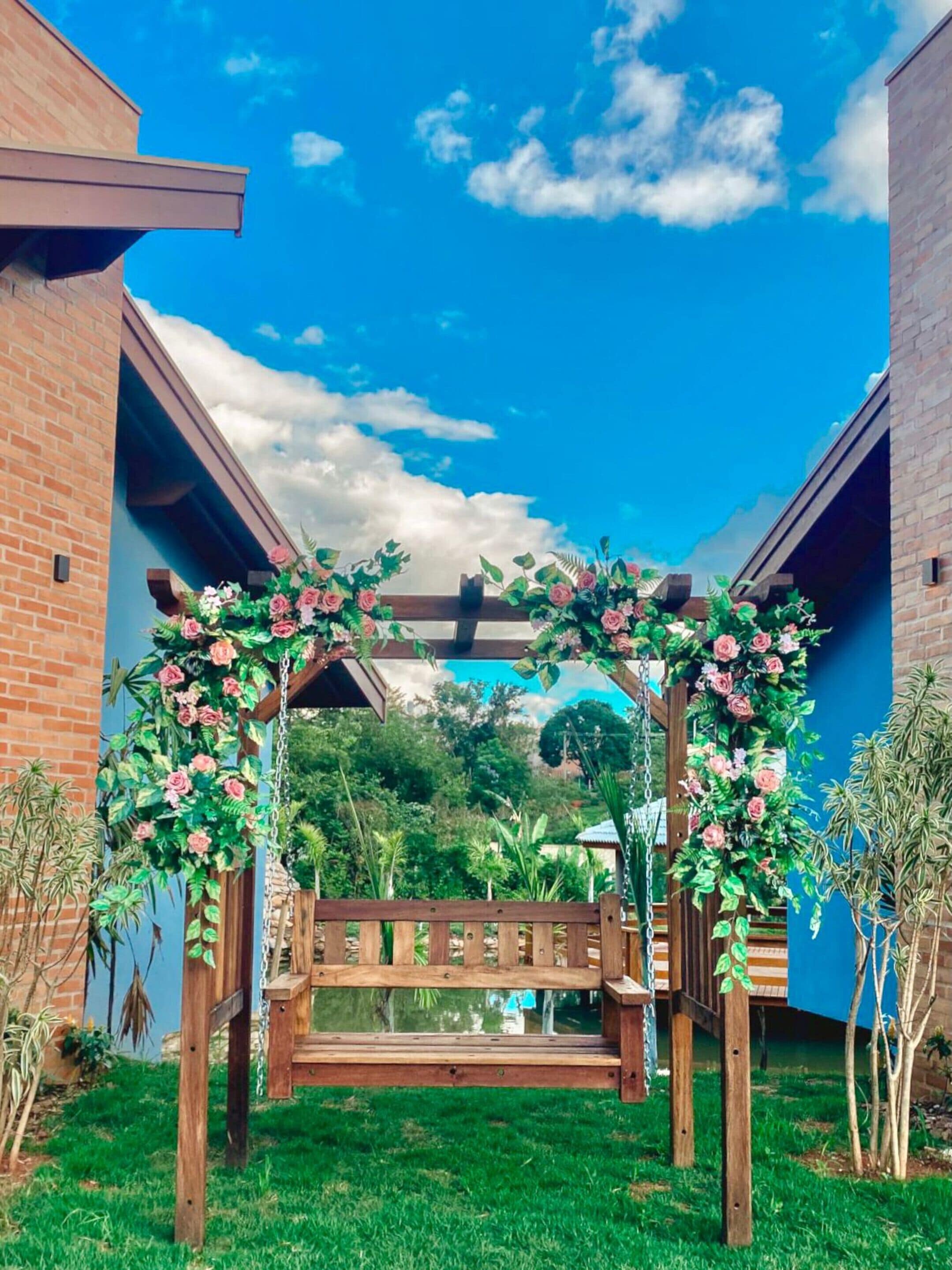 A wooden bench under a floral archway in a courtyard with brick buildings and greenery.